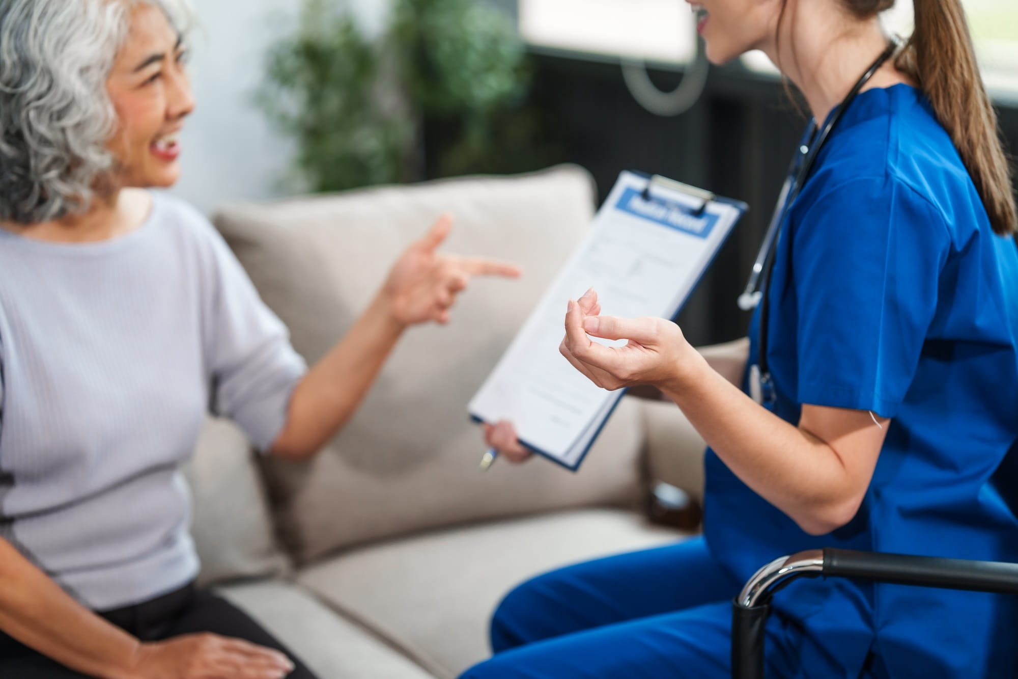 Caucasian female doctor delivers the results health check elderly Asian patient both seated sofa